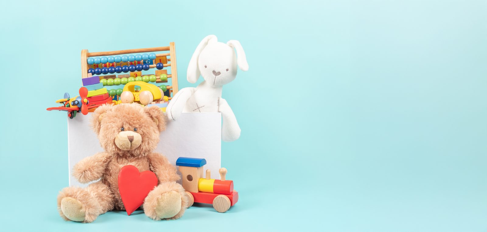 A toy box of wooden educational toys and a teddy bear on a light blue background
